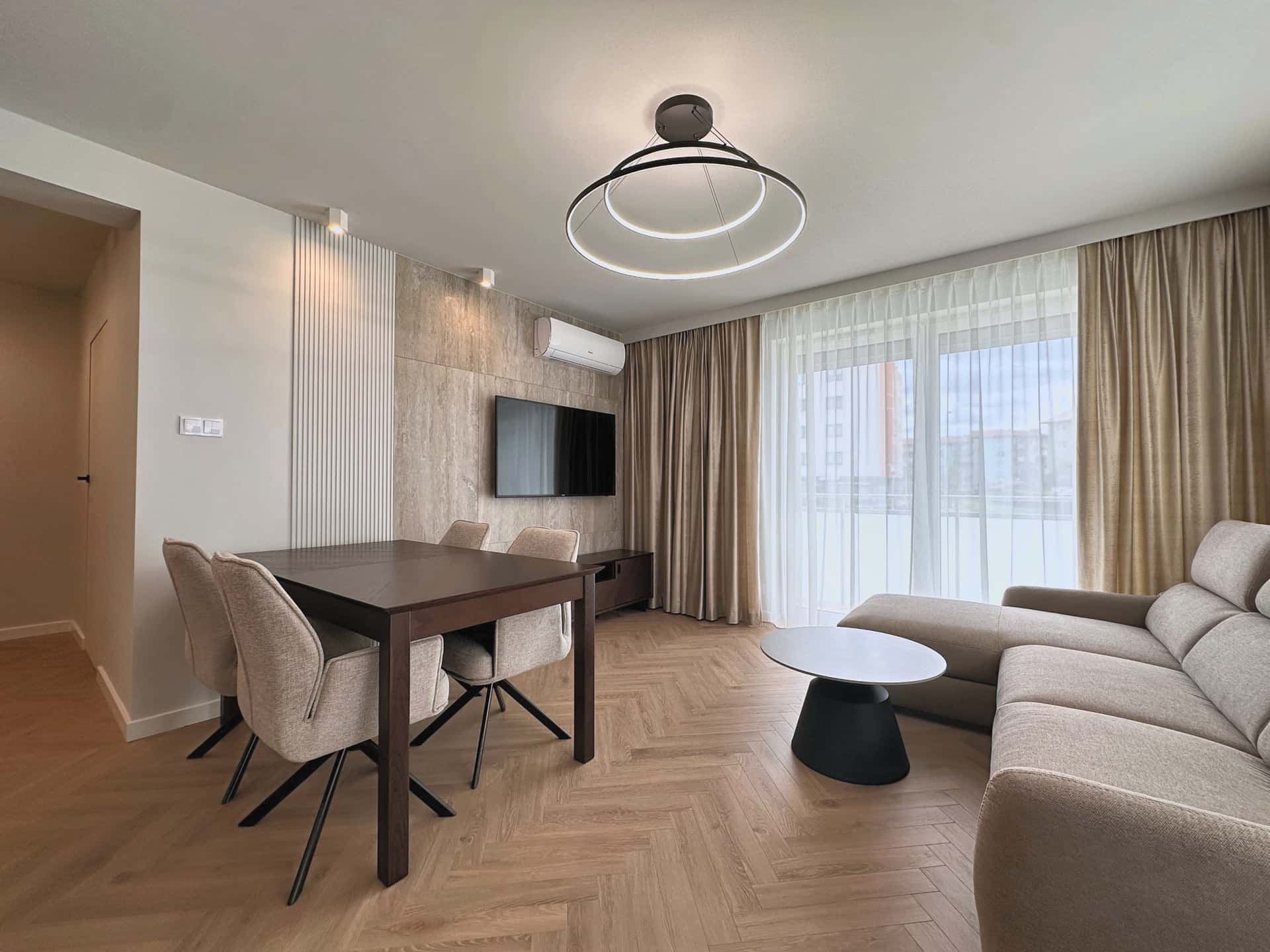 Salon z jadalnią po wykończeniu mieszkania 65 m² w Zielonej Górze: ściana TV z płytkami o rysunku trawertynu, białe lamele i podłoga w jodełkę